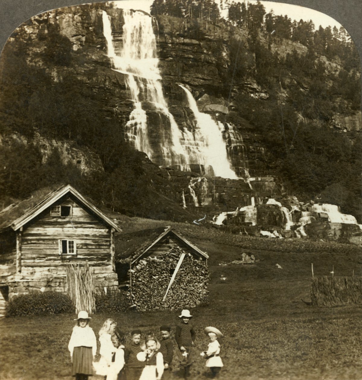 Børn leger på en bondemark med terrasseret Tvinde-vandfald, Vossevangen, Norge, c1905. af Unbekannt