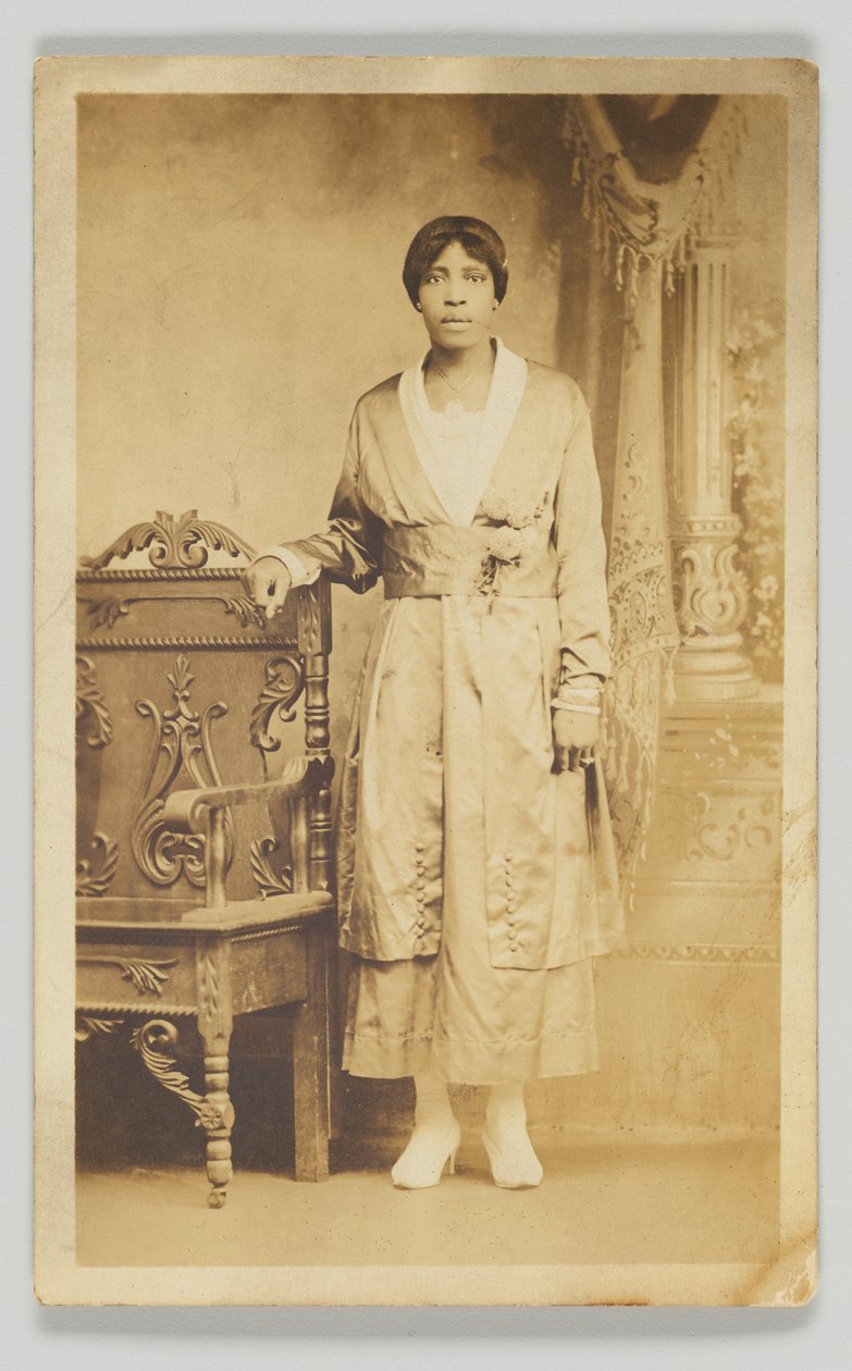 Fotografisk postkort af en kvinde stående ved siden af en træstol, 1904-1918. af Unbekannt