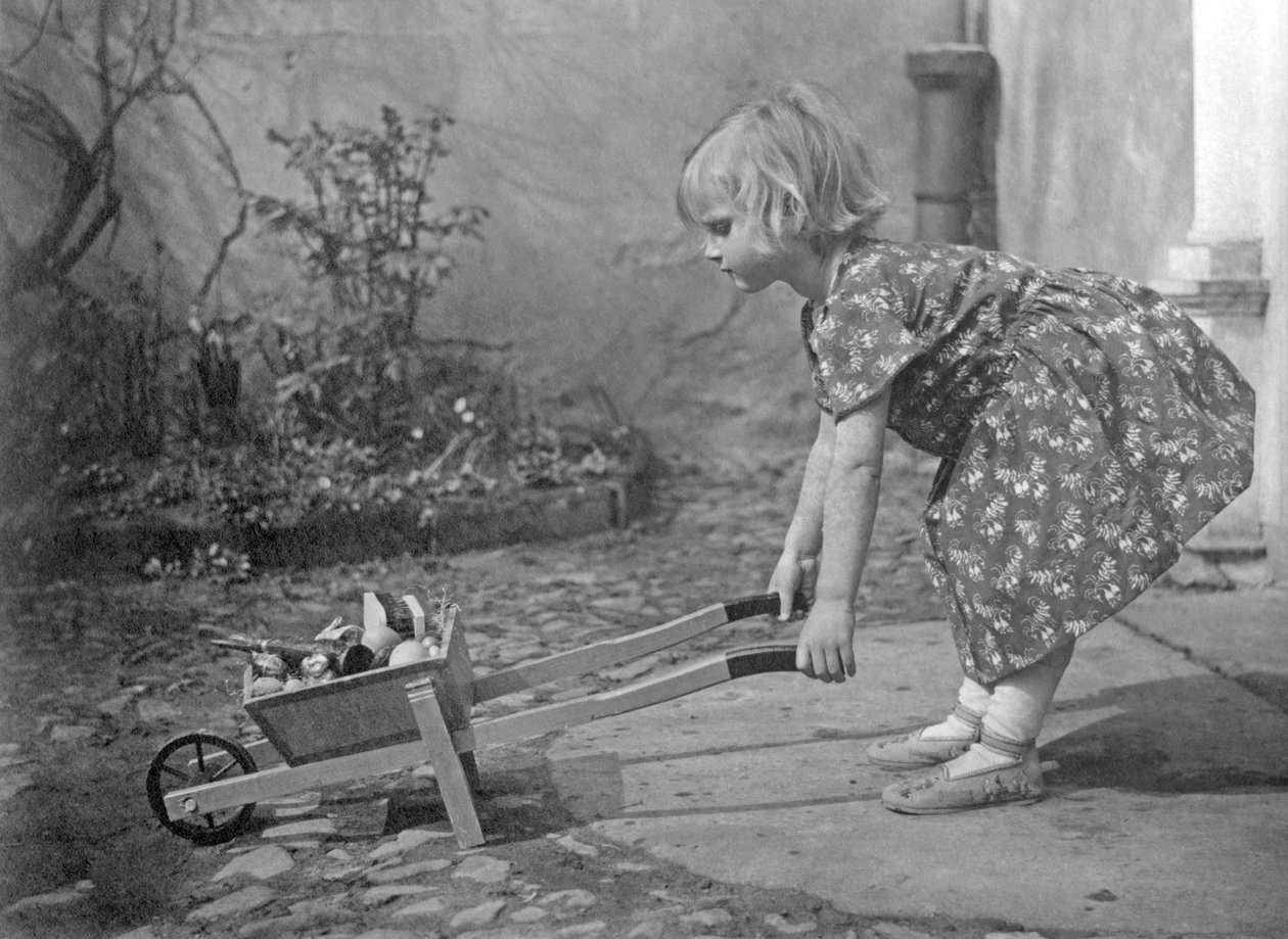 Lille pige leger med en trillebør. Fotografering omkring 1931 af Unbekannt