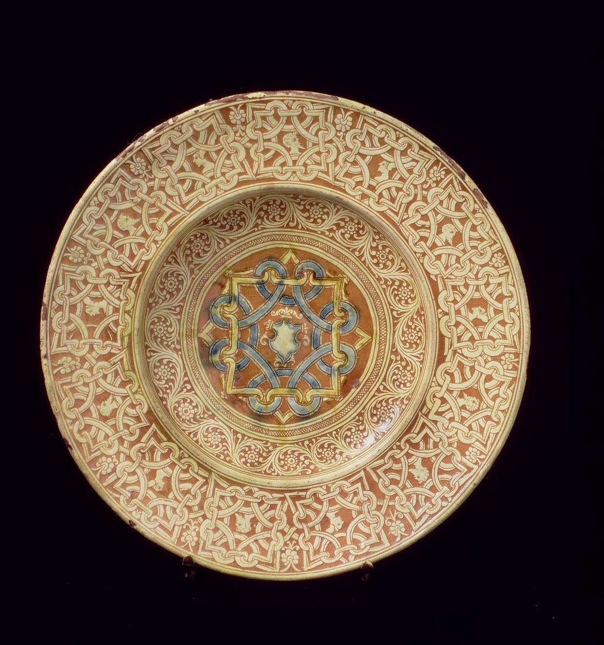 Maiolica tallerken dekoreret med et kunstfærdigt gentagne knudedesign, der rammer profilhoveder på kanten og et skjold i den centrale plakette, italiensk, lavet i Toscana af Unknown