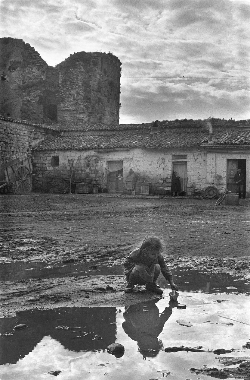 Ung pige leger med en papirbåd i en vandpyt omgivet af mudder, Venosa, Basilicata, Italien af Unbekannt