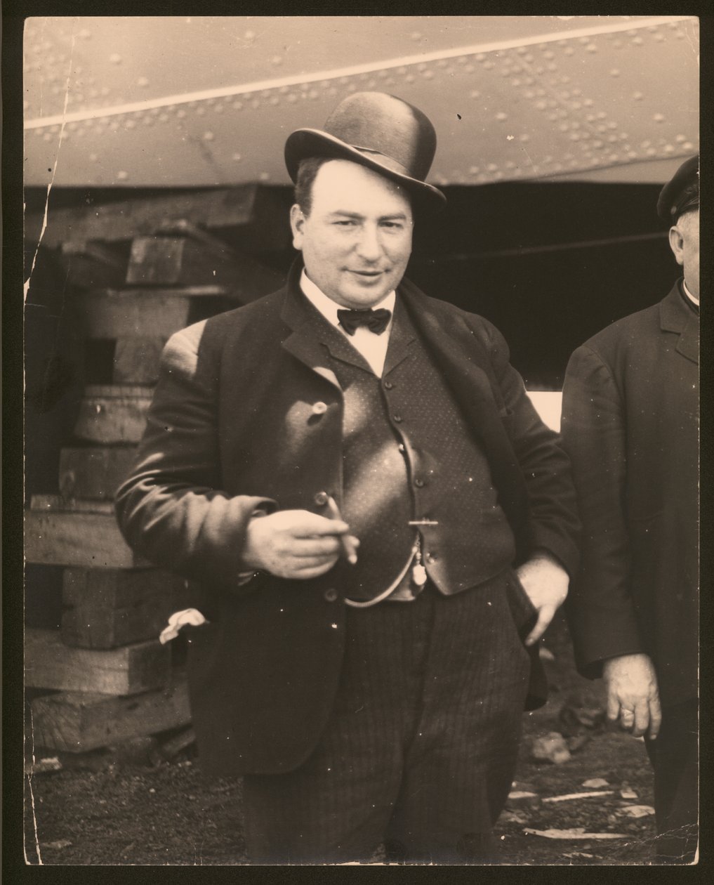 Lodret, sort / hvidt fotografi af en mand i en derbyhue og sløjfe, der ryger en cigar af William G. Swekosky