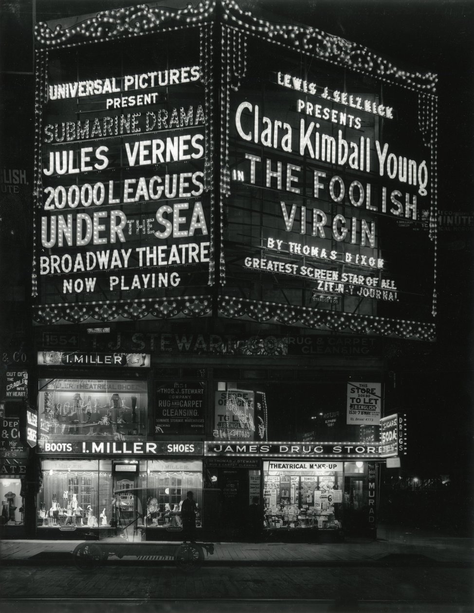 1554 Broadway på 46th Street, I. Miller Shoes; James Drug Store, og store markiser til film lyser op ovenfor. af William Davis Hassler