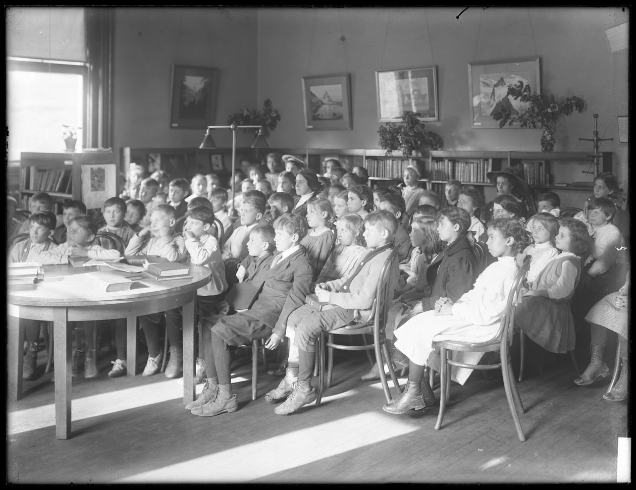 Børn siddende og lyttede i læsesalen i en uidentificeret afdeling af Queens Borough Public Library, ca. 1910 af William Davis Hassler