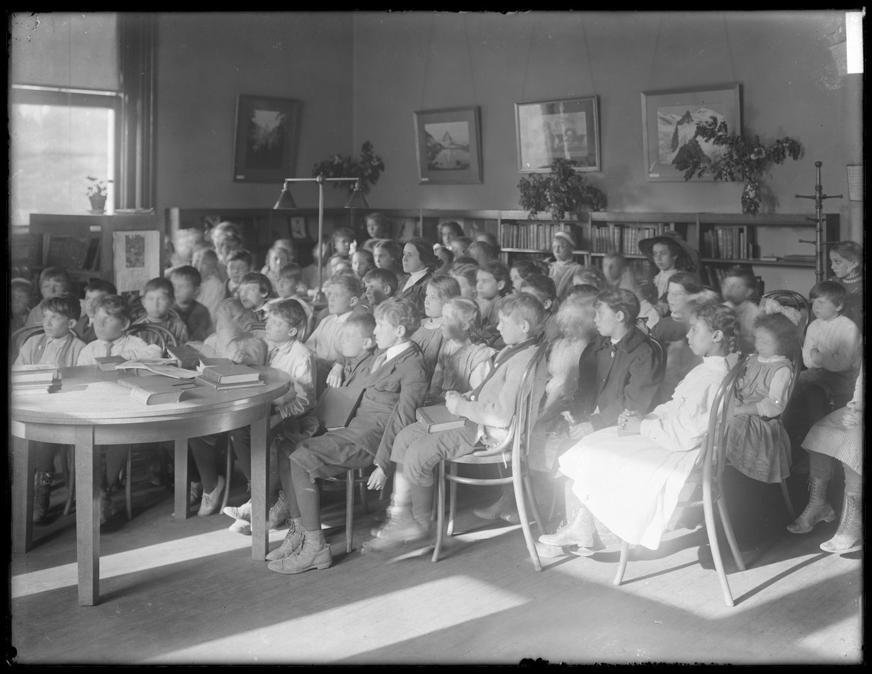 Børn siddende og lyttede i læsesalen i en uidentificeret afdeling af Queens Borough Public Library, ca. 1910 af William Davis Hassler