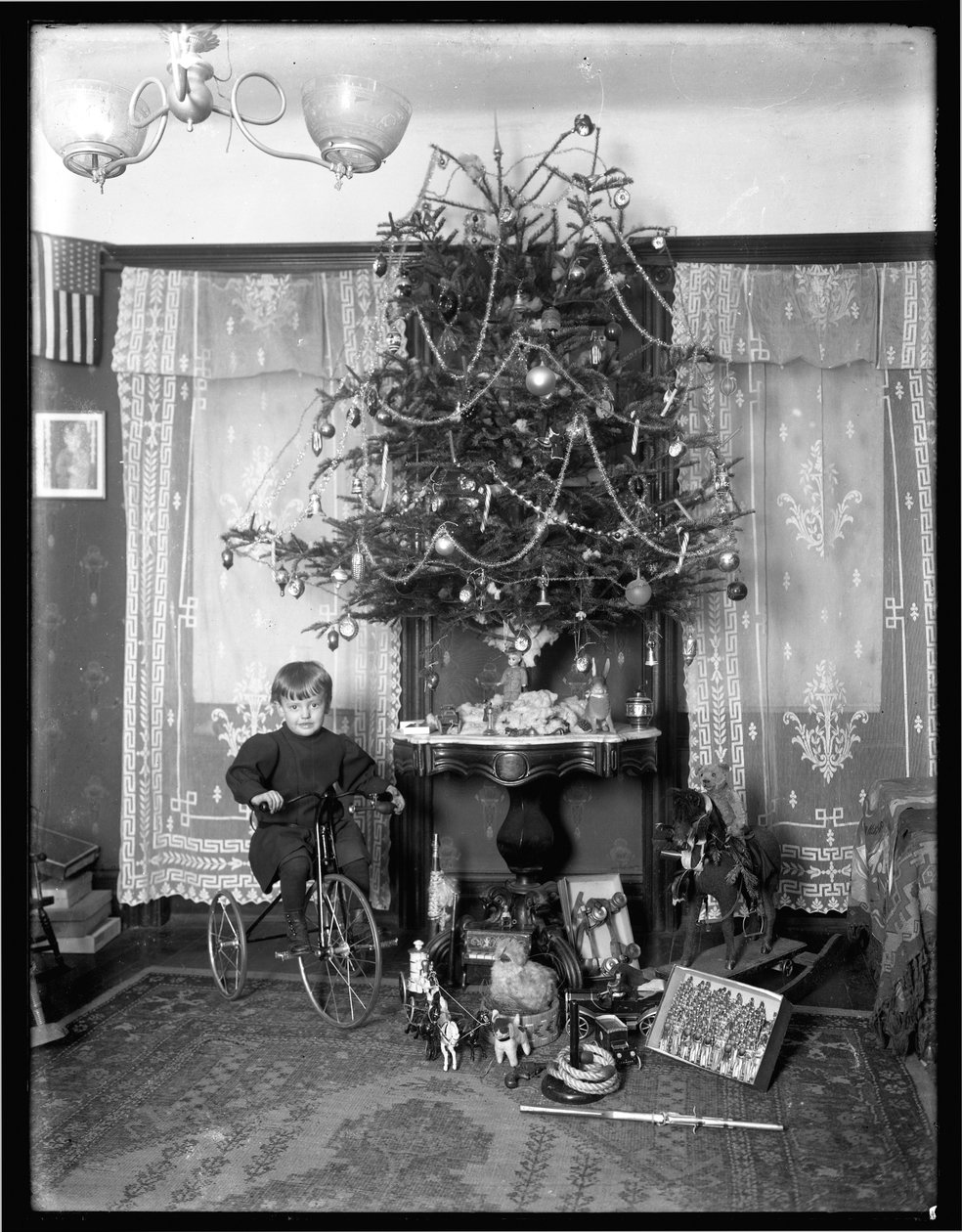 Seymour-dreng poserede siddende på trehjulet cykel ved siden af juletræet i stuen, julen 1912 af William Davis Hassler