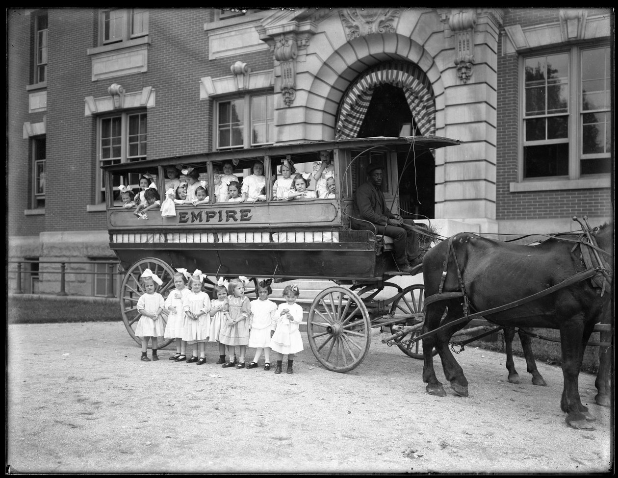 Små piger poserer i og foran en hestevogn foran en uidentificeret bygning, sandsynligvis det romersk-katolske forældreløse asyl, Kingsbridge, Bronx, ca. 1910 af William Davis Hassler