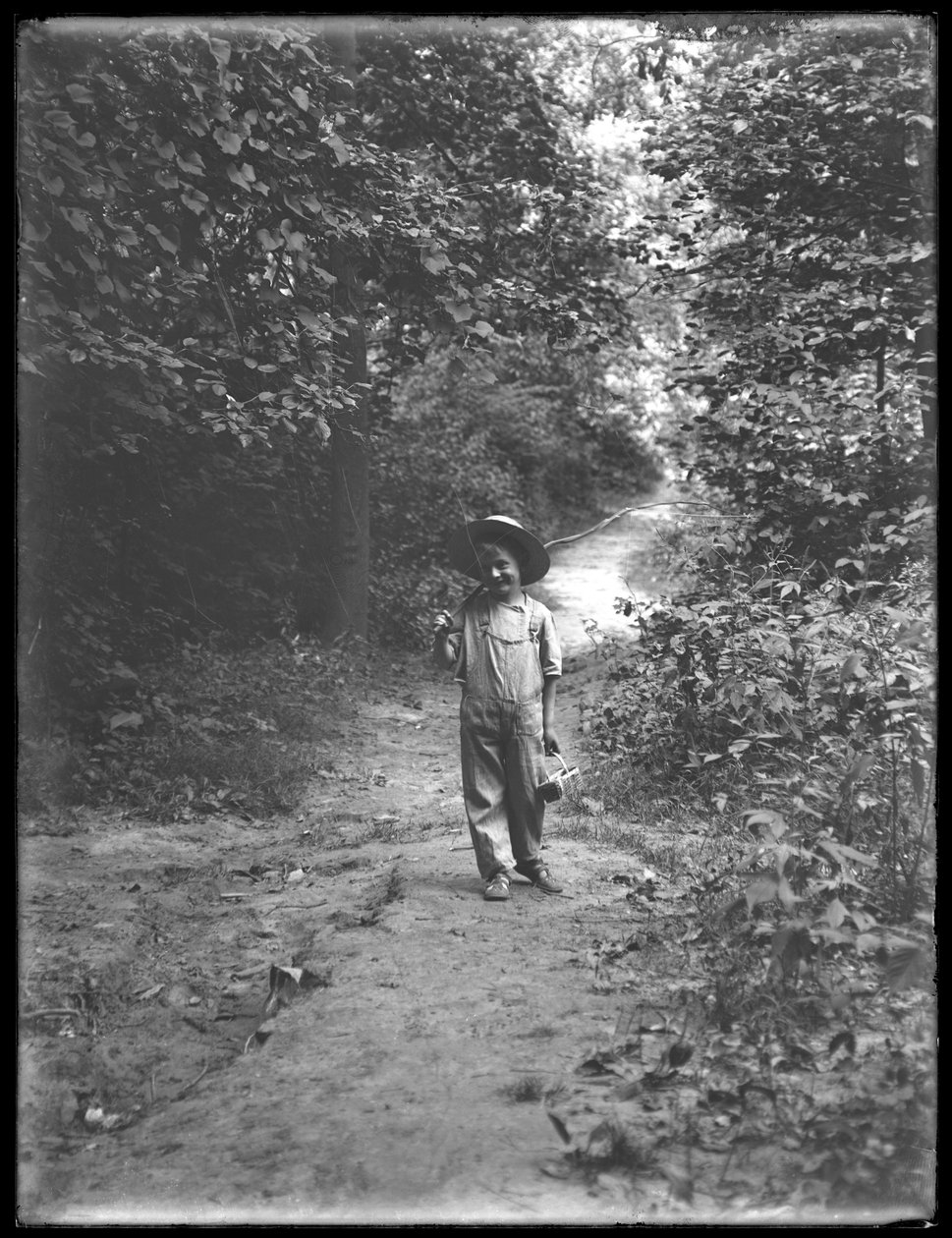 William Gray Hassler i stråhat og overalls, bærende fiskestang og kurv, gående ned ad en sti i skoven alene, 20. august 1911 af William Davis Hassler