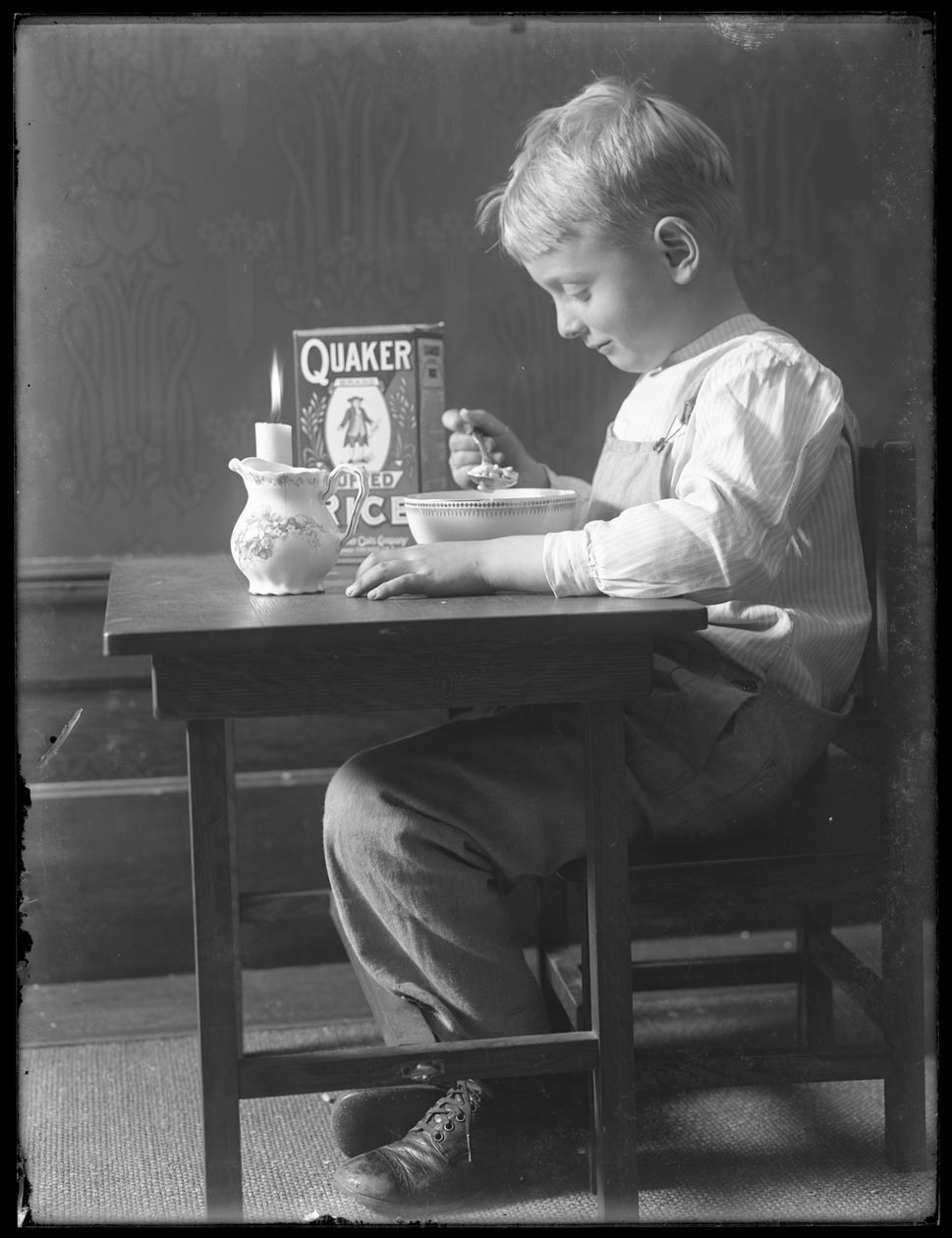 William Gray Hassler sad ved et lille bord og spiste en skål Quaker puffed ris, ca. 1912 af William Davis Hassler