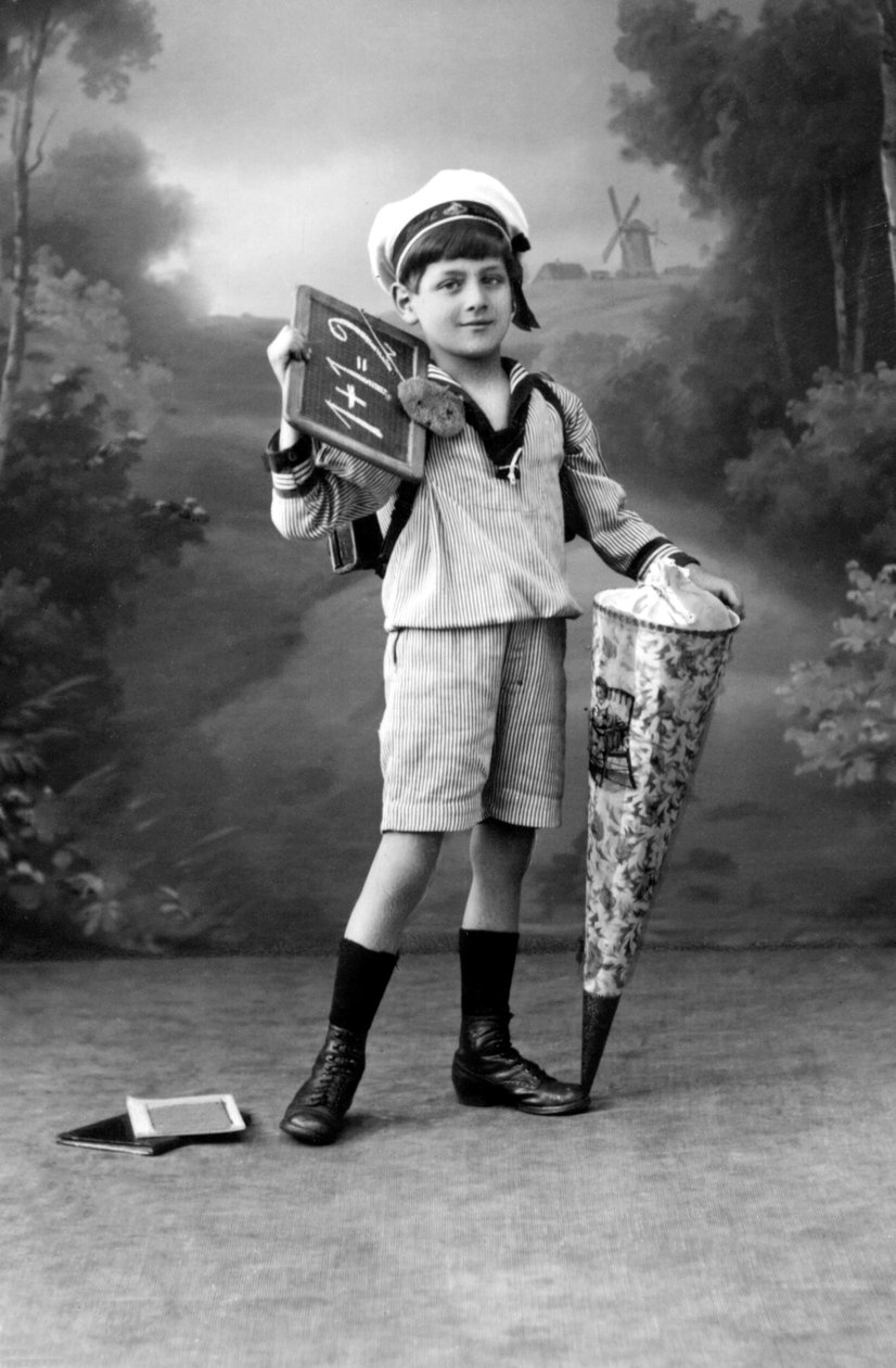 Første skoledag. En ung dreng i uniform poserer med en tavle med tilføjelsen 1+1 = 2 og en overraskelsespose. Fotografering omkring 1910. af Ferdinand Georg Waldmuller