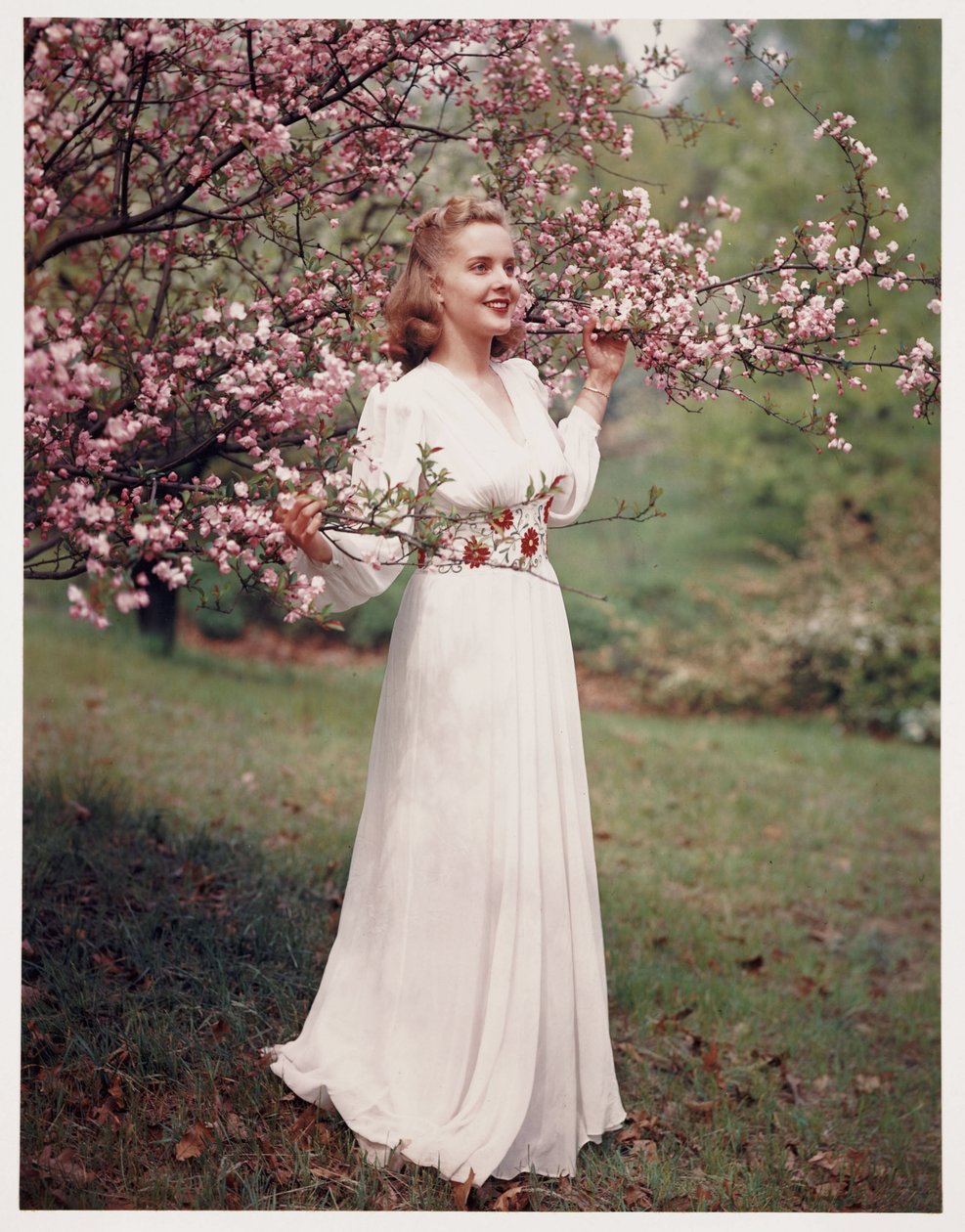 Kvinde modellerer en kjole nær blomstringen, ca 1940