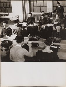 [Folk sidder foran skrivemaskiner med hovedtelefoner på].