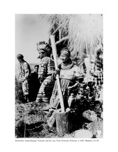 Annie Jumper Tommie brugte en morter og støder til at lave majsmel, og hendes søn, Tony Tommie, iført en ørnefjerhjelm, 5. februar, 1927