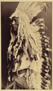 Gammel person, Piegan. Unge mænd går ikke glip af nogen anledning til offentlige festligheder for at tage deres krigerfars tøj på. Foto taget fra bind 6 af encyklopædien udgivet af Edward S. Curtis (1868-1952) om indianerne i Nordamerika, med en forgrund af Edward Sheriff Curtis