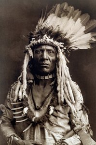 Væselhale (Apohsuyis). Portræt af indianerhøvdingen af Piegan-stammen bærer den berømte ørnefjer og væsel hovedbeklædning, en ruskinds-tunika, to halskæder, den ene i ben og den anden i grizzly-kløer, og en tomahawk-pibe af Edward Sheriff Curtis