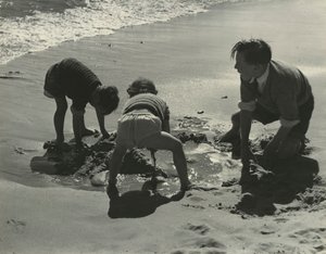 Tre børn leger med sand på stranden.