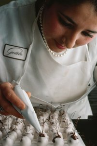 En Godiva-kok sætter chokoladestilke på fondantovertrukne kirsebær. Bruxelles, Belgien. af James L Stanfield