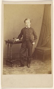 [Uidentificeret lille dreng i jakkesæt står ved et bord med bøger ovenpå]. af Joseph Brown