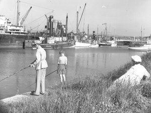 En mand og en dreng fisker i Glasson Dock, mens en dame sejler; havlandskab; en mand bagved ser på, forskellige både ligger fortøjet af Joseph Hardman