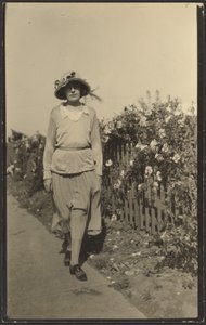 [Kvinde går langs hegn med blomster]. af Louis Fleckenstein