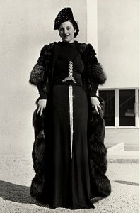 Model i aftenkjole skabt af det italienske couture-hus "Dragoni". Artiklens skrifttype har en prangende pailletdekoration i form af et sværd. En hat og pelsoverfrakke fuldender ensemblet. (s/h foto)
