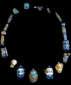Halskæde i glaspasta med vedhæng, der forestiller skæggede hoveder, oprindeligt fra Olbia, nu konserveret på Cagliari National Archeological Museum