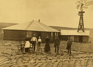 Familie af husmænd uden for deres torvhus med en vindmølle på taget af den tilstødende bygning i Custer County, Nebraska, ca. 1885 (s/h-foto) af Solomon D. Butcher