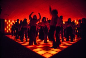 Unge dansere på et diskotek, der danser på et oplyst gulv. af Ted Spiegel