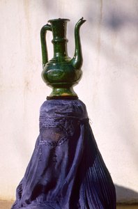 En kvinde i Kabul, der er skjult af et silketørklæde, chadri, bærer en kande fra en...