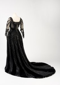 Sort aftenkjole i fuld længde båret af dronning Alexandra, med dekoration af perler og pailletter og inkorporeret dronning Alexandras signaturnavnebånd i sort silke og guld, lavet af Barolet fra Knightsbridge, London 1908-1910 (silke og fløjl) af Unbekannt