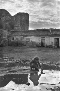 Ung pige leger med en papirbåd i en vandpyt omgivet af mudder, Venosa, Basilicata, Italien af Unbekannt