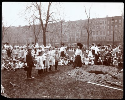 Voksne og børn holder flag stående omkring et nygravet hul til en træplantning på Arbor Day i Tompkins Square Park, New York, 1904 (sølv gelatinetryk) af Byron Company