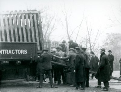 En flok tilskuere står ved siden af, mens et næsehorn bliver læsset af en lastbil af vogtere i London Zoo i 1924 af Frederick William Bond