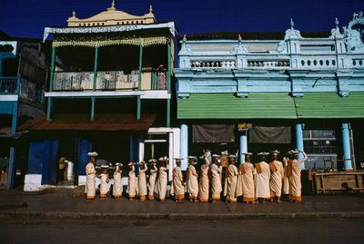 Buddhistiske nonner i forskellige aldre paraderer på fortovet og beder om almisser. Maymyo, Burma. af James L Stanfield