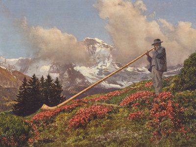 Schweiz: En alpehornsblæser, Jungfrau i baggrunden (farvefoto) af Jean Gaberell
