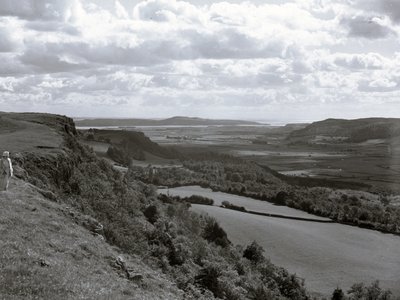 En dame står på en bjergskråning og kigger ud over landskabet ved Scout Scar. af Joseph Hardman