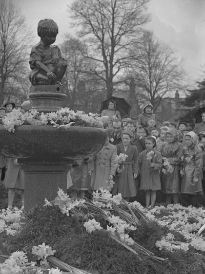 Børn lægger klaser af påskeliljer på springvand med statue på toppen af Joseph Hardman
