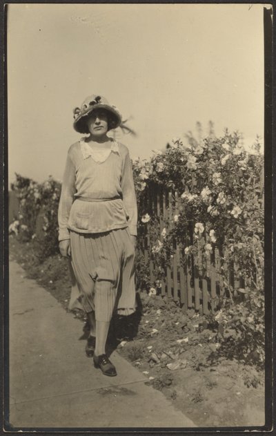 [Kvinde går langs hegn med blomster]. af Louis Fleckenstein