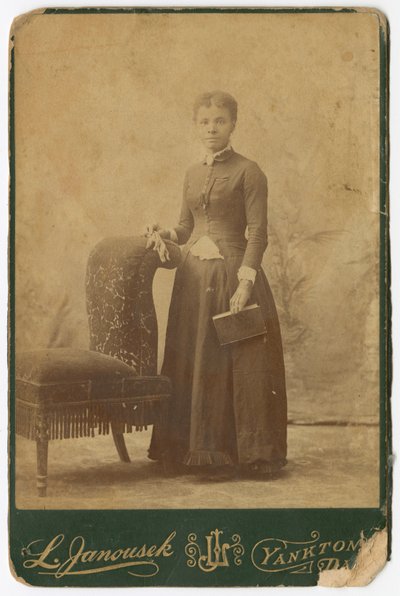 Fotografi af en kvinde, der står ved siden af en stol og holder en bog, slutningen af det 19. århundrede. af Louis Janousek