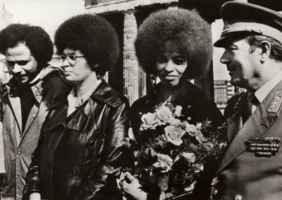 Den 11. september 1972 blev den modige amerikanske kommunist og borgerrettighedsforkæmper Angela Davis hilst hjerteligt velkommen af soldaterne fra Den Tyske Demokratiske Republiks Nationale Folkehær ved Brandenburger Tor (s/h foto) af Photographer German