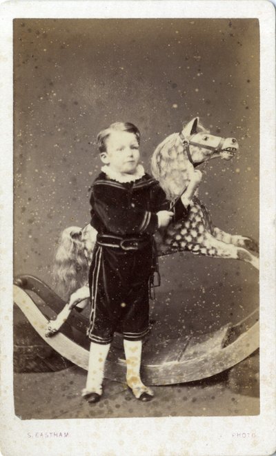 Ung dreng stående ved en gyngehest af Silas Eastham
