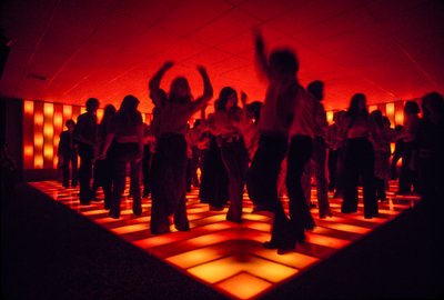 Unge dansere på et diskotek, der danser på et oplyst gulv. af Ted Spiegel