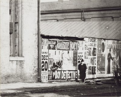En mand går forbi en væg med plakatannoncer, herunder en til Johnnie Hoey The Boy Detective, der spiller på Havlins teater på 600 Walnut Street. af Unbekannt