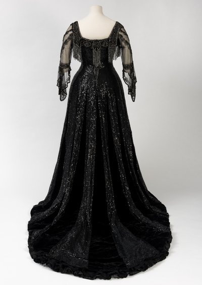 Sort aftenkjole i fuld længde båret af dronning Alexandra, med dekoration af perler og pailletter og inkorporeret dronning Alexandras signaturnavnebånd i sort silke og guld, lavet af Barolet fra Knightsbridge, London 1908-1910 (silke og fløjl) af Unbekannt