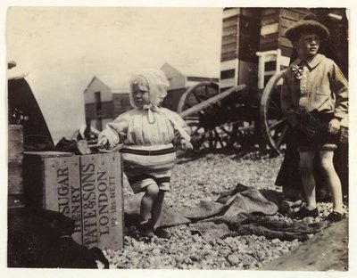 To børn ved bademaskiner, c 1895, Et øjebliksbillede af to børn ved havet, stående blandt en gruppe bademaskiner på stranden af Unbekannt