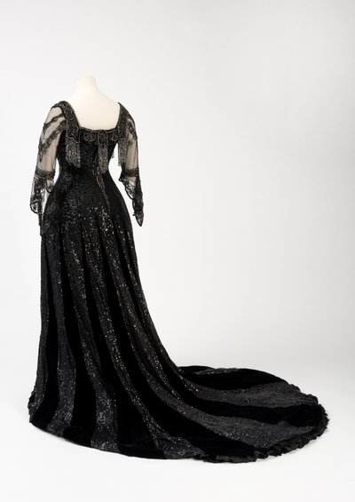 Sort aftenkjole i fuld længde båret af dronning Alexandra, med dekoration af perler og pailletter og inkorporeret dronning Alexandras signaturnavnebånd i sort silke og guld, lavet af Barolet fra Knightsbridge, London 1908-1910 (silke og fløjl) af Unbekannt