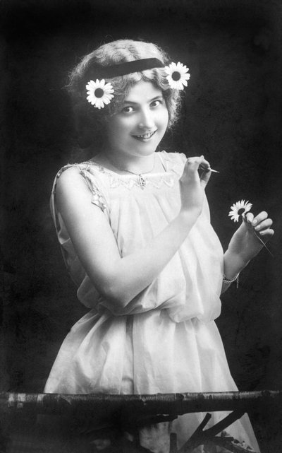 Kvinde trækker kronblade fra en blomst: "" Han elsker mig. Han kan ikke lide mig. Han elsker mig...” Fotografering omkring 1912 af Unbekannt