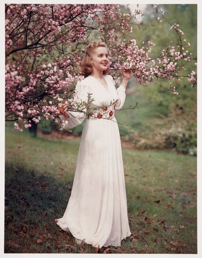 Kvinde modellerer en kjole nær blomstringen, ca 1940