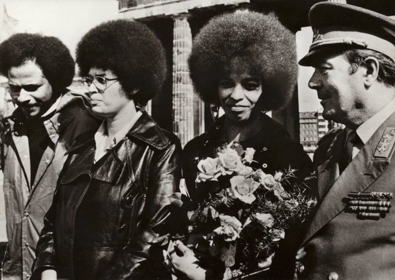 Den 11. september 1972 blev den modige amerikanske kommunist og borgerrettighedsforkæmper Angela Davis hilst hjerteligt velkommen af soldaterne fra Den Tyske Demokratiske Republiks Nationale Folkehær ved Brandenburger Tor (s/h foto) af Photographer German
