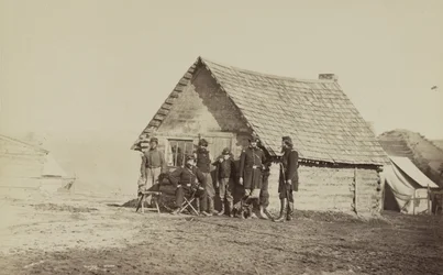 En gruppe soldater og to unge mænd, den ene en afroamerikaner, står uden for bjælkehyttekvarteret, 1861-65